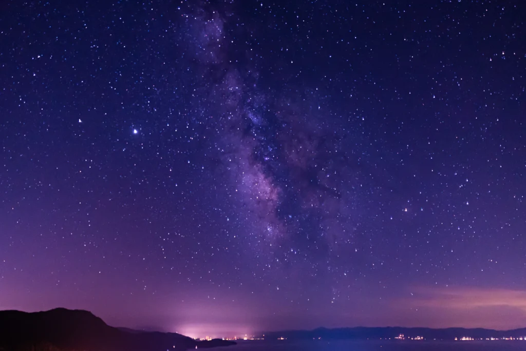 Star-filled night sky above a dark mountain landscape, the sky a natal chart maps